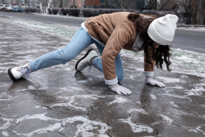 Woman slipping and falling on icy sidewalk as an example of a winter hazard, illustrating the importance of preventing slip and fall accidents in snowy and icy conditions.